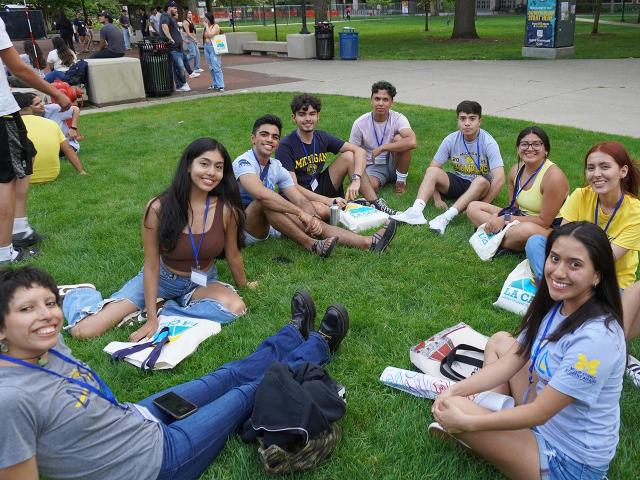 Welcome program participants seated in a circle on the lawn near the Diag
